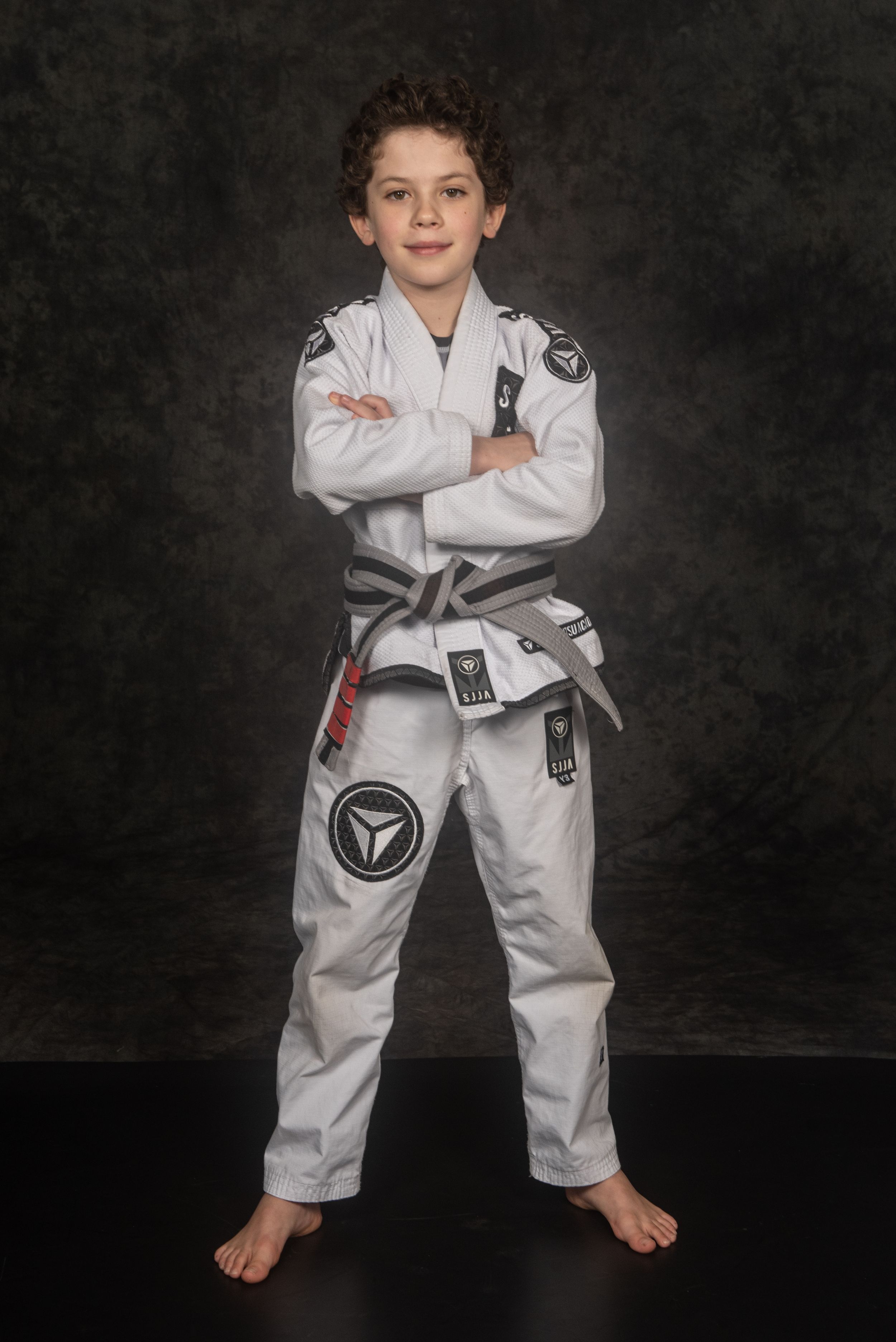 Young martial artist in white uniform posing confidently against dark backdrop.
