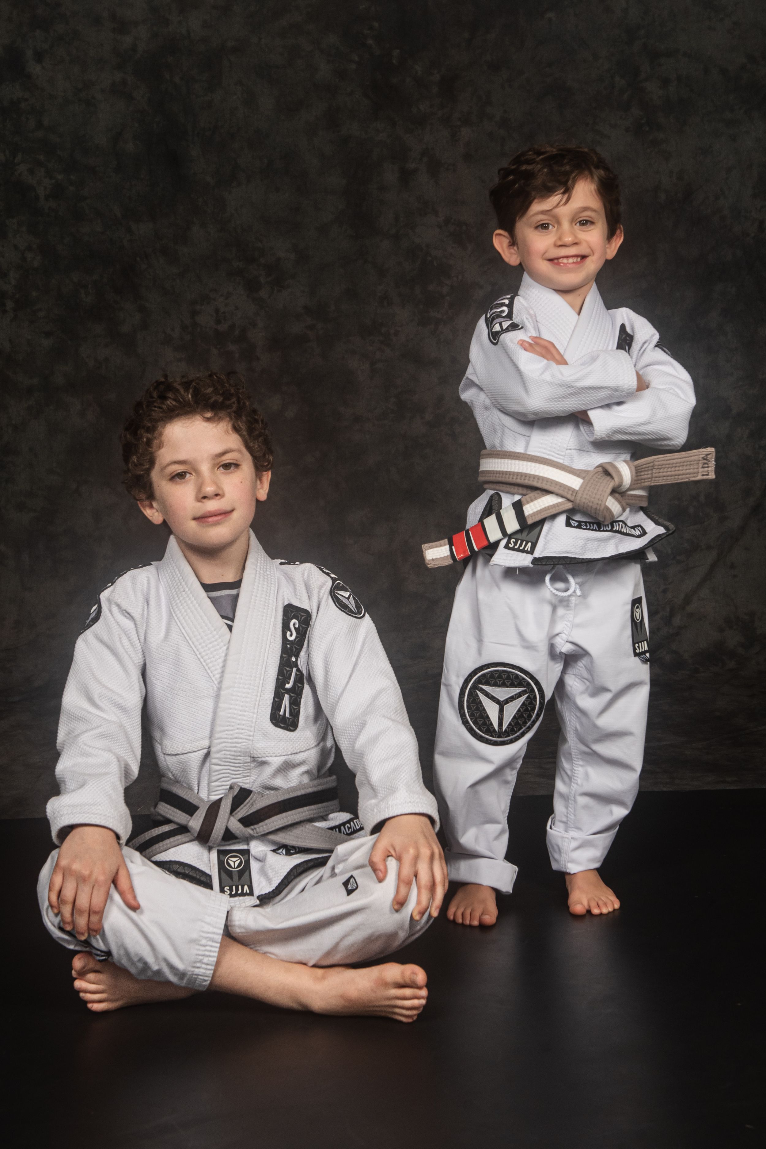 Two martial arts students in white uniforms pose together on a dark background.