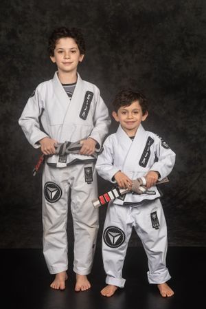 Two martial arts practitioners in white gis stand barefoot together against a dark backdrop.