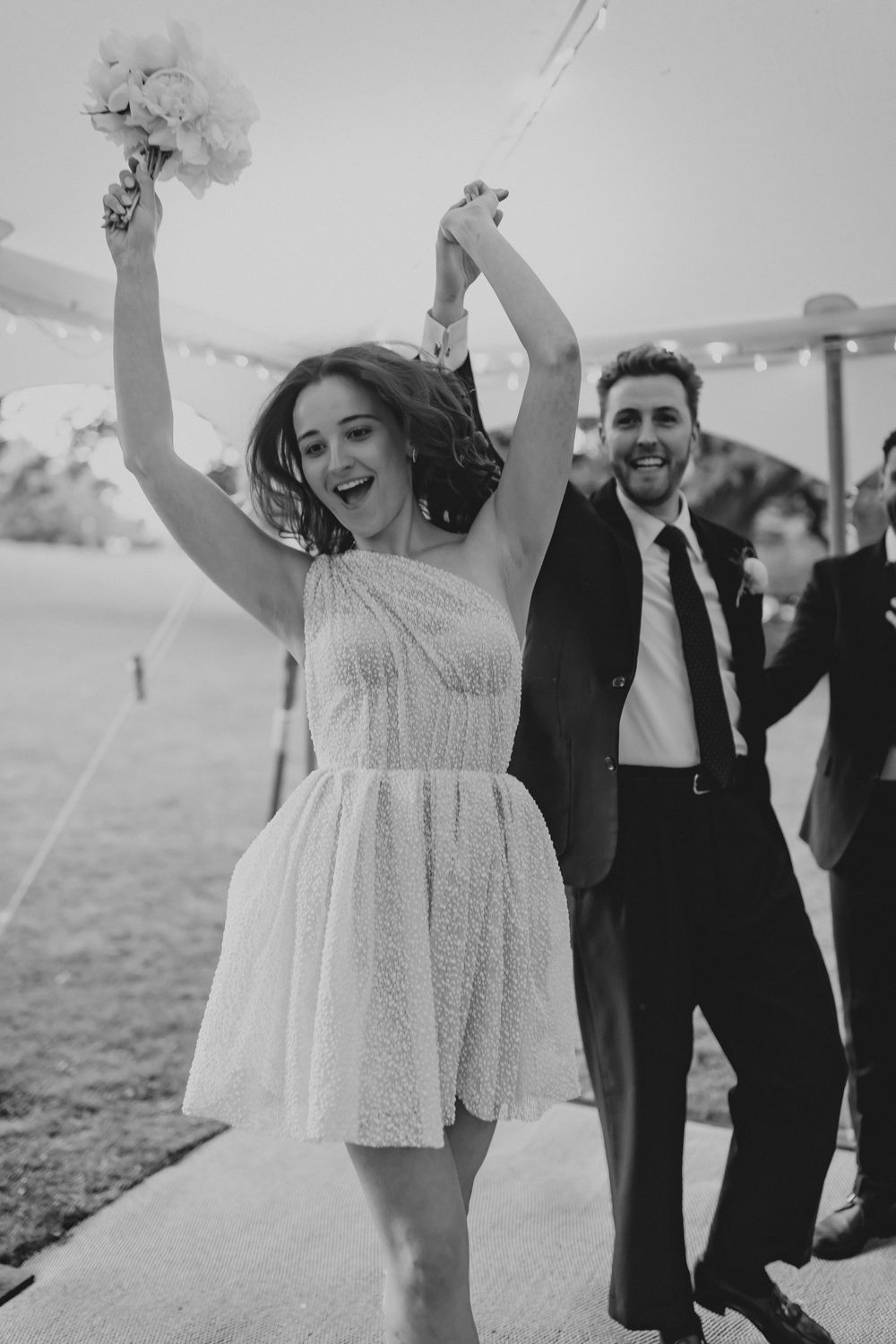 Joyful wedding celebration with people dancing and raising arms in black and white photography.
