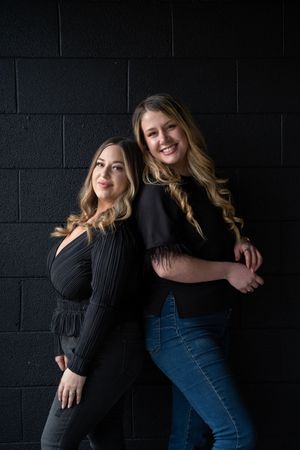 Women in dark clothing posing casually against a black wall.