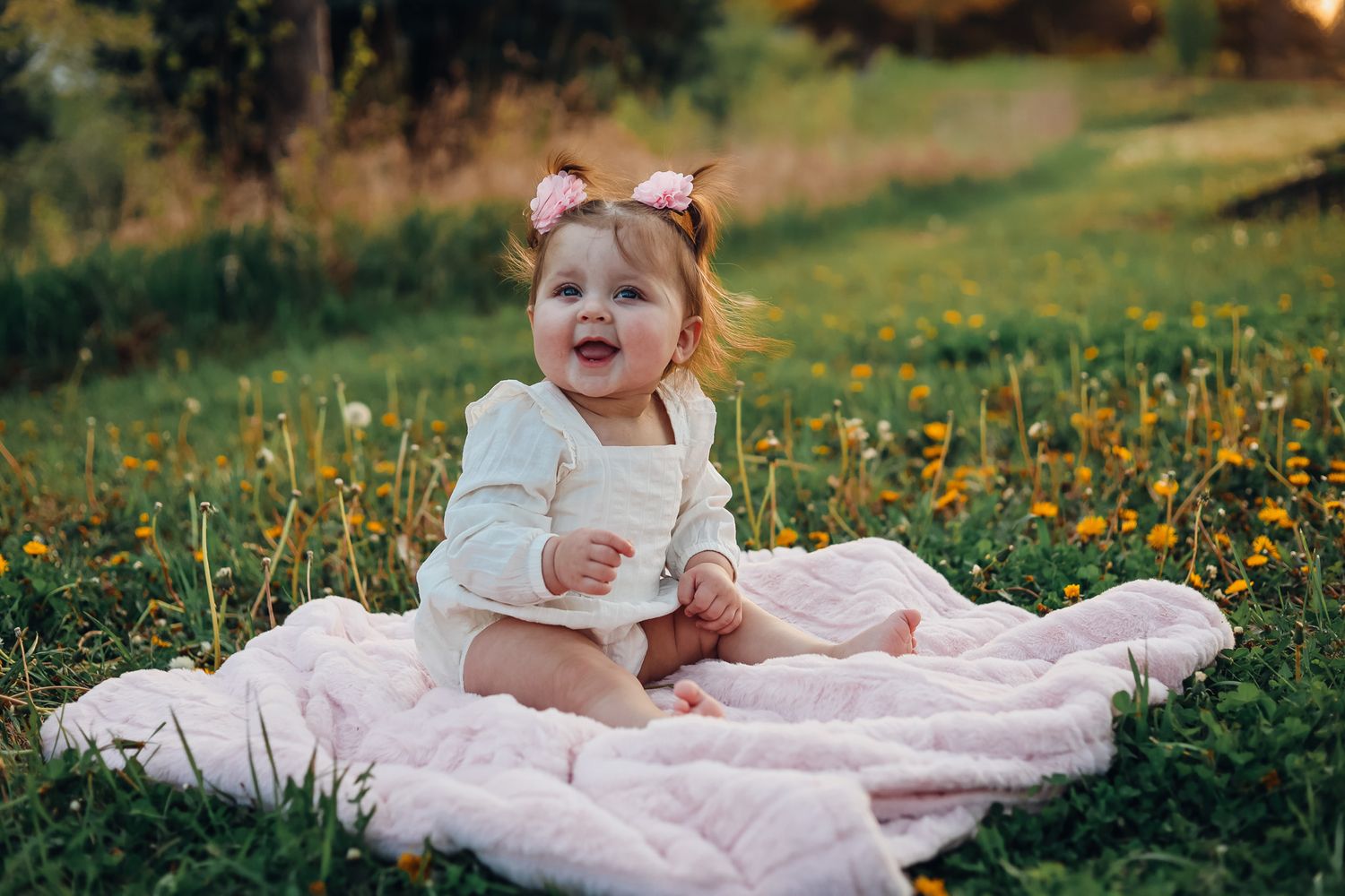 Baby in blue dress sitting among vibrant yellow wildflowers. Example of a milestone photography sessions