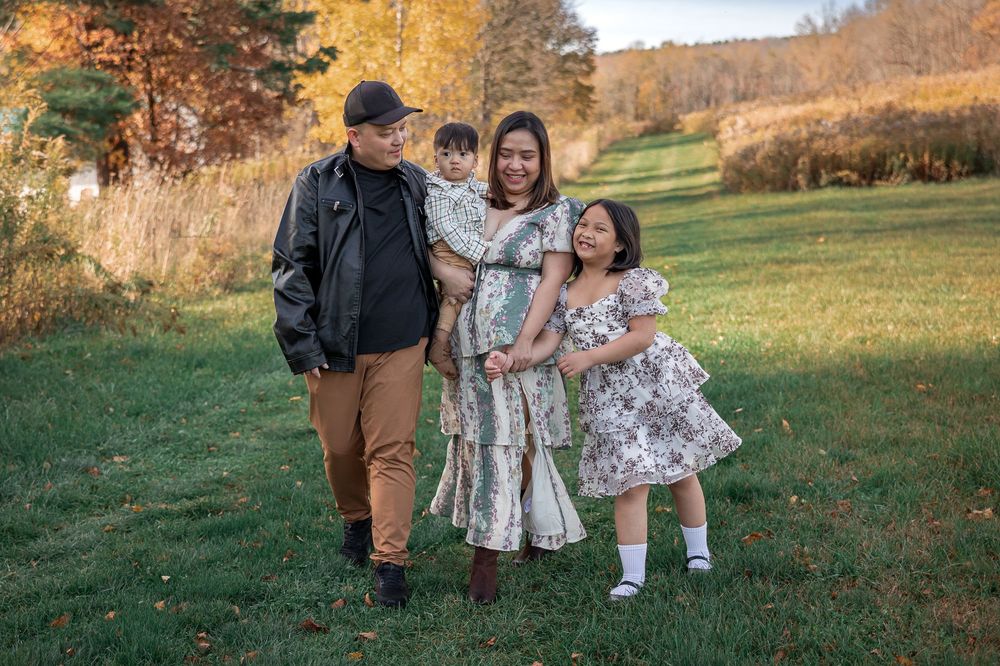 Family in coordinated outfits walking through autumn field during golden hour sunset photoshoot.