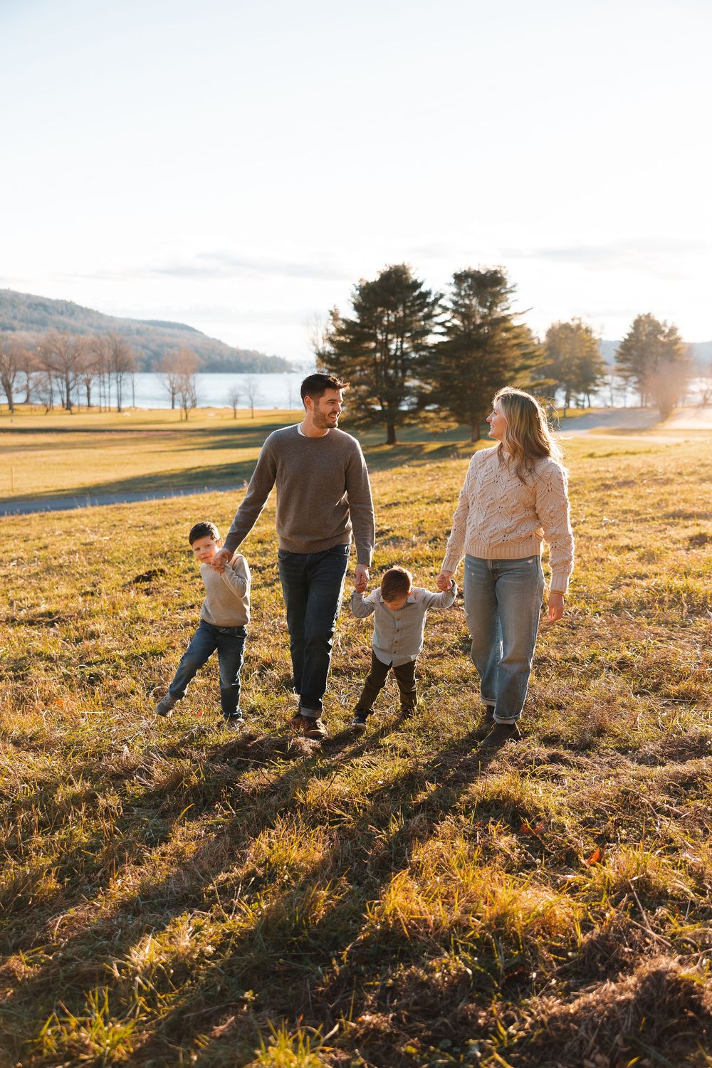 Family walking together on a golden grass field near a lake during sunset with mountains in the background.