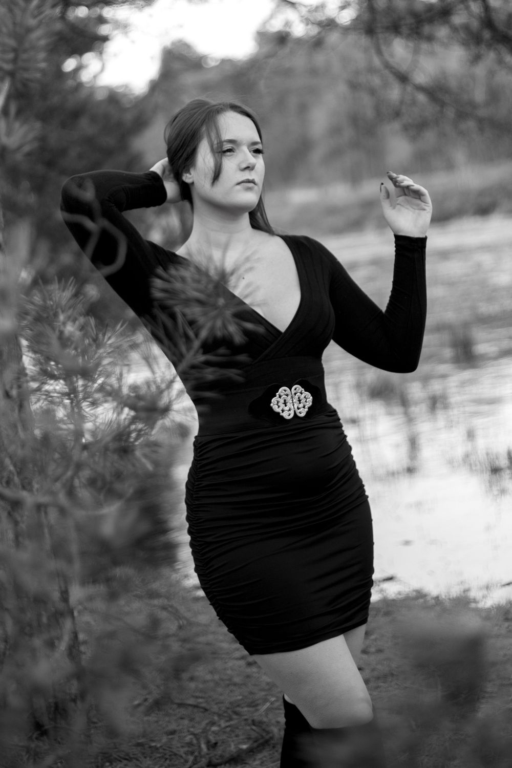 Black and white portrait of a figure in an elegant black dress with a decorative brooch posing outdoors.