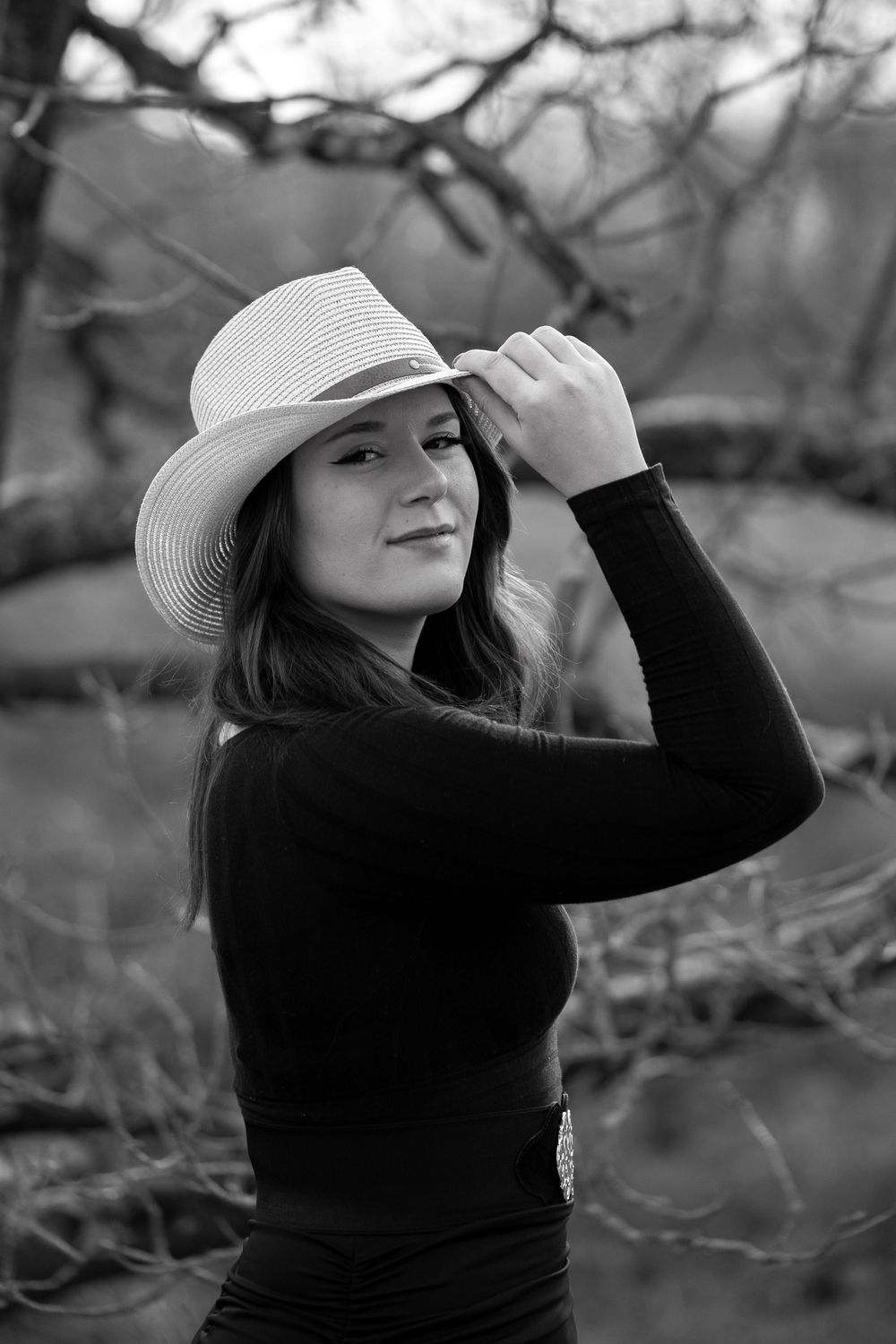 Black and white portrait of a woman wearing a white cowboy hat and black sweater outdoors in moody lighting.