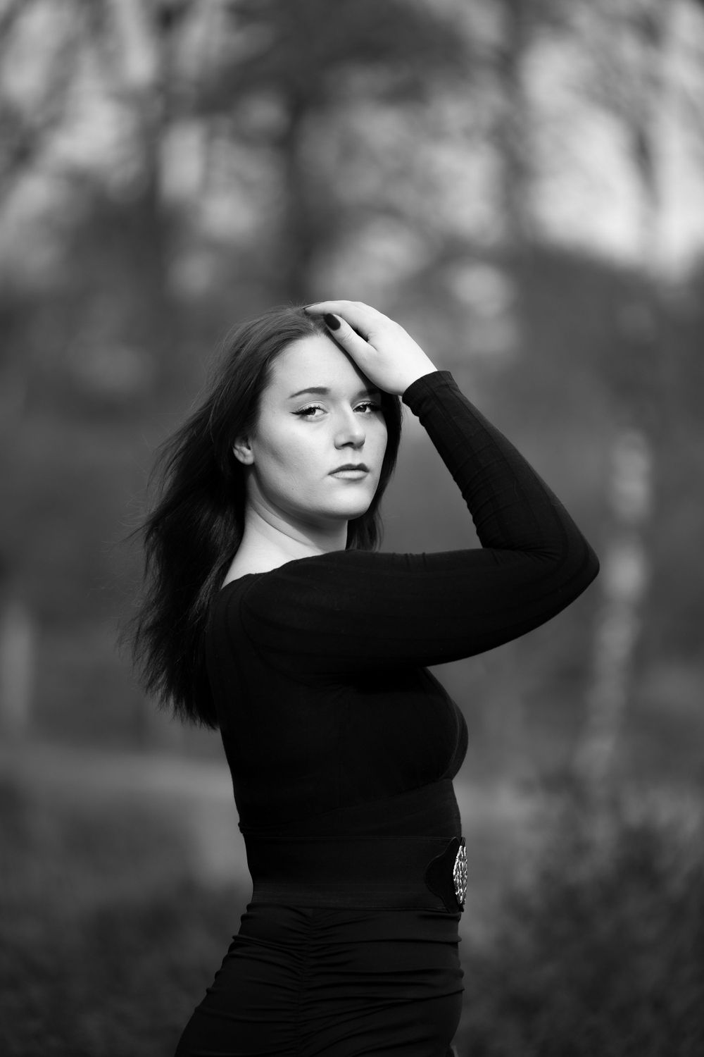 Artistic black and white portrait of a person in a black sweater posing against a blurred forest background.
