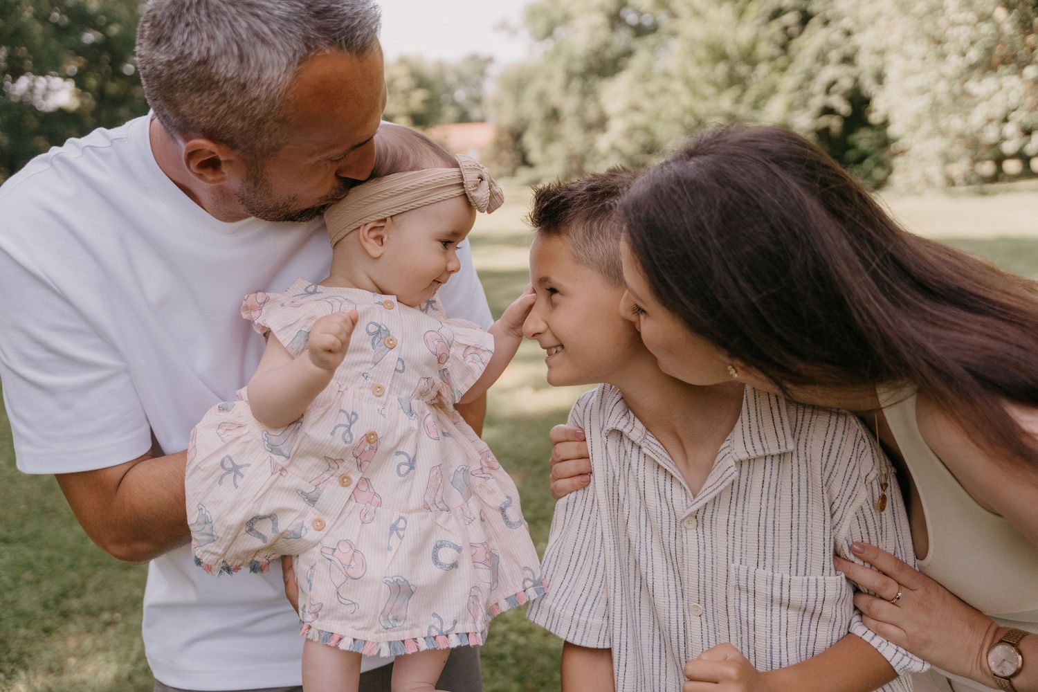 Eine Familie teilt einen intimen Moment im Freien, lehnt sich eng aneinander und hält ein Baby in einem rosa geblümten Kleid im Arm.