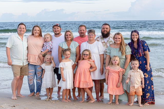 Large family group in coordinated outfits posing together on beach at sunset.