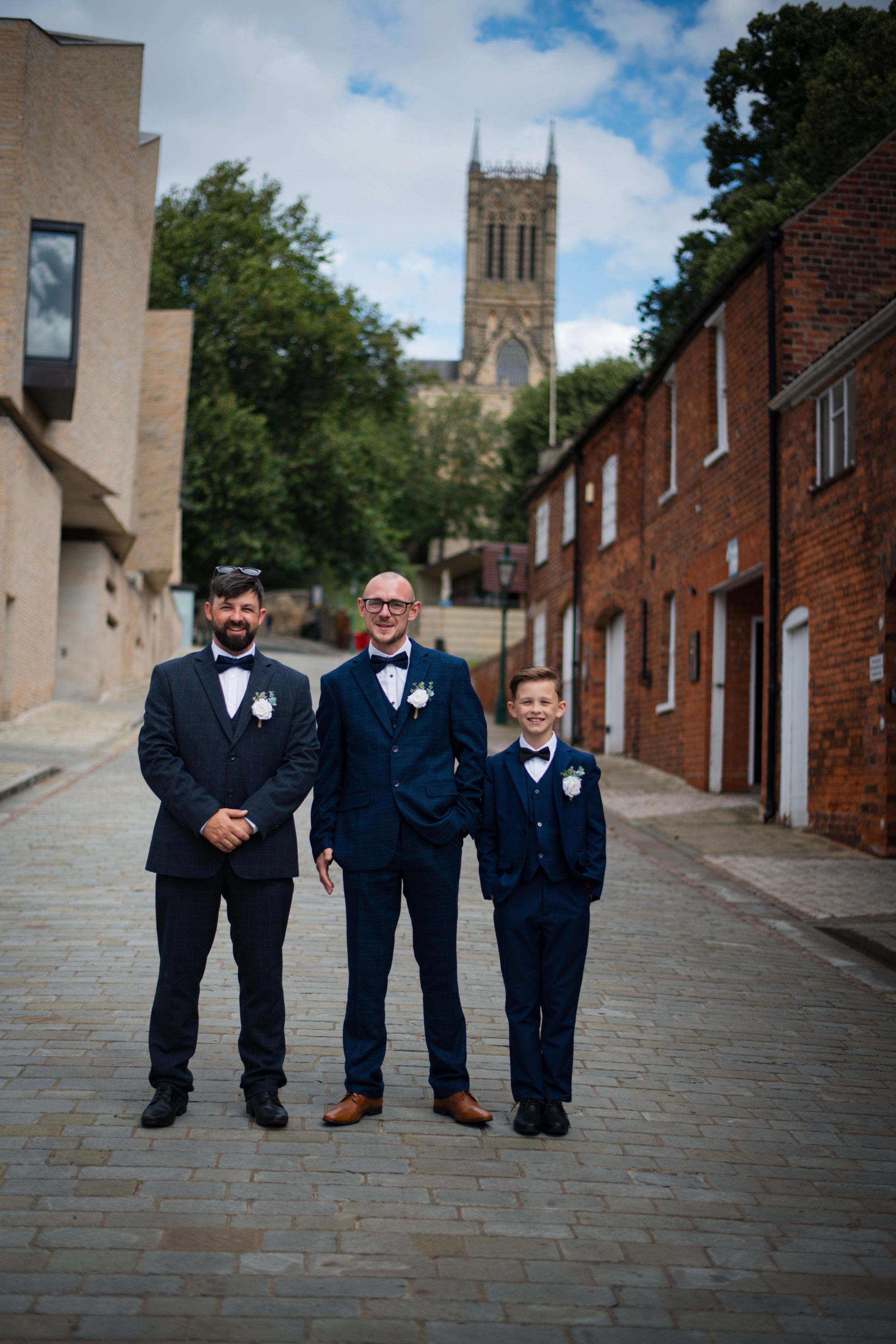 Three people in matching navy suits stand on cobblestone street with cathedral in background.