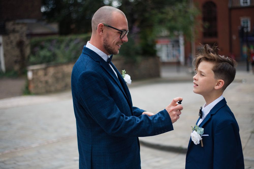 Formal moment between two people in navy suits adjusting boutonniere outdoors.