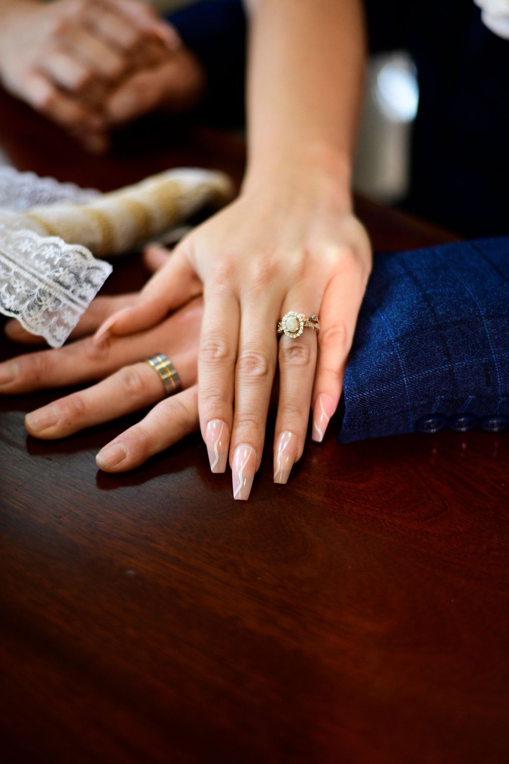 Close-up of manicured hand with engagement ring resting on dark wooden surface.