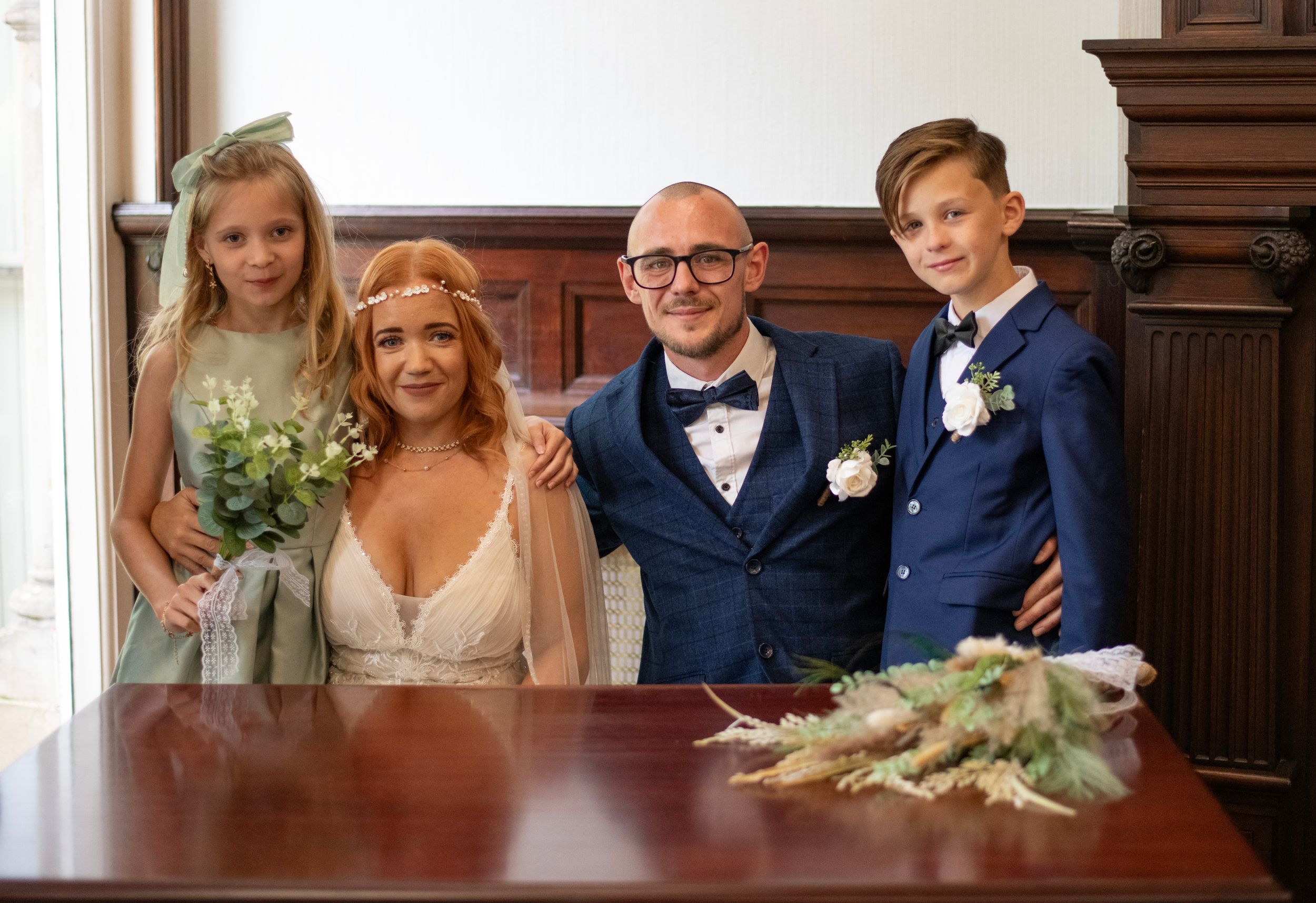 Wedding party poses together with elegant attire and floral bouquets at an indoor venue.