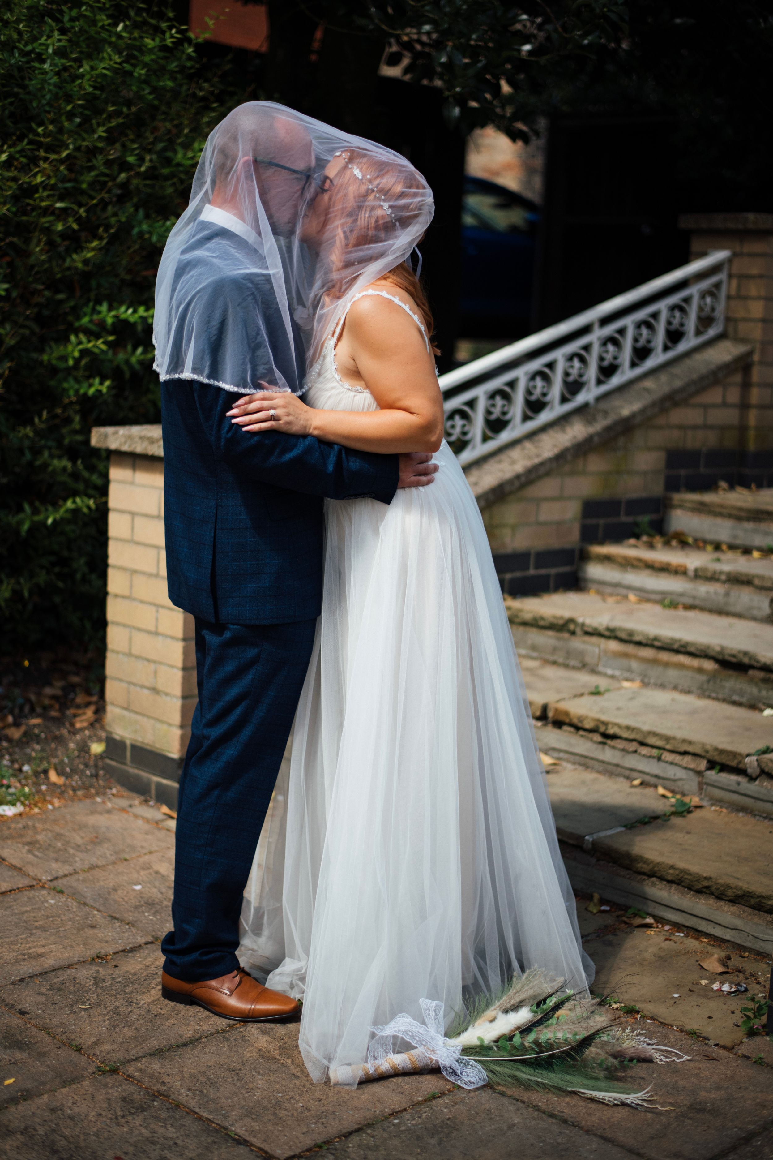 Newlyweds share an intimate moment under a veil on stone steps.