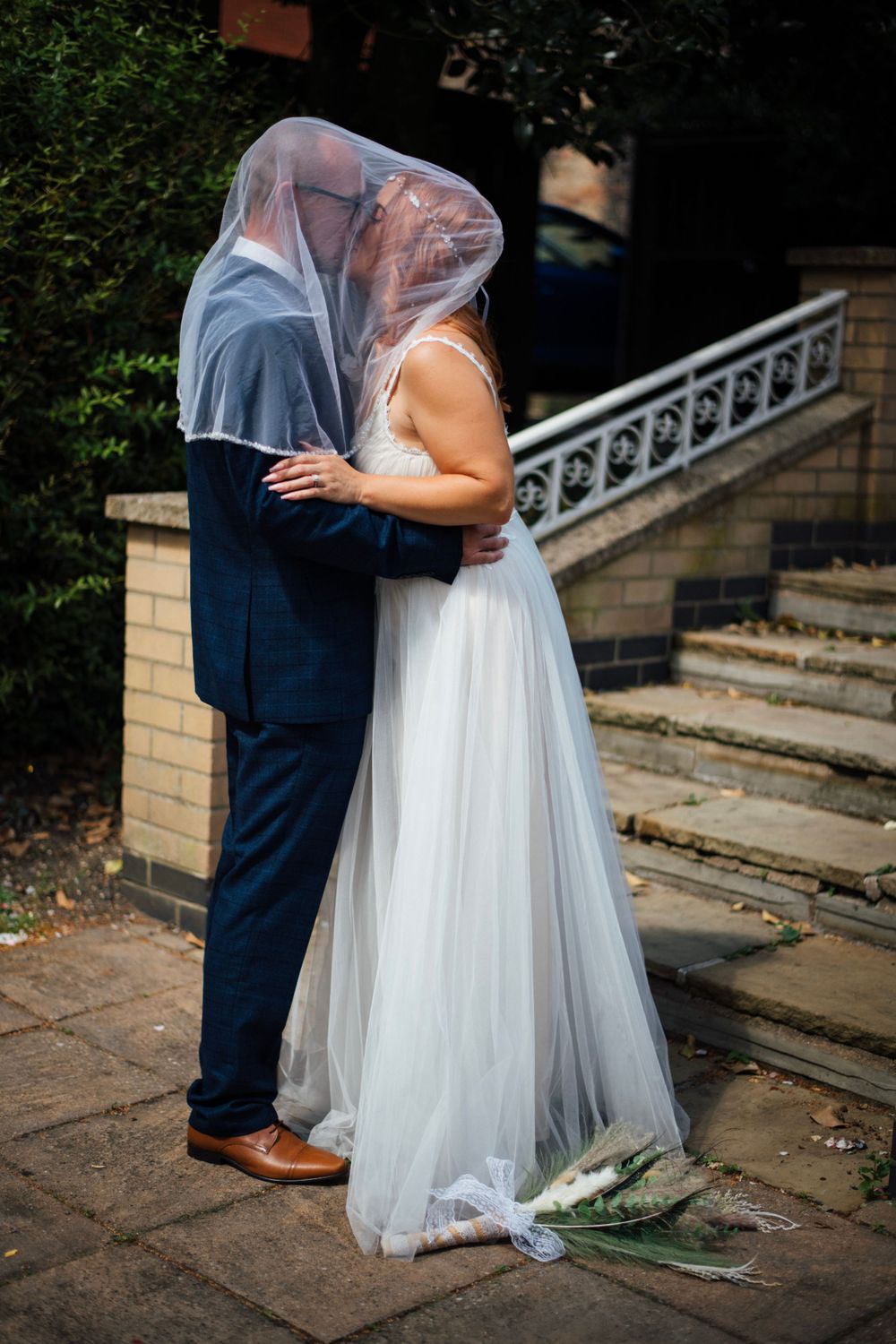 Newlyweds share an intimate moment under a veil on stone steps.