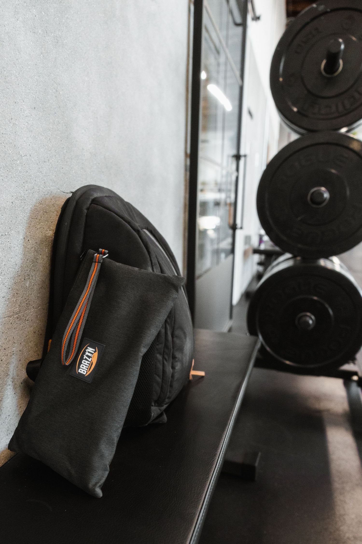 Black backpack rests on workout bench with weight plates mounted on wall in background at fitness gym.