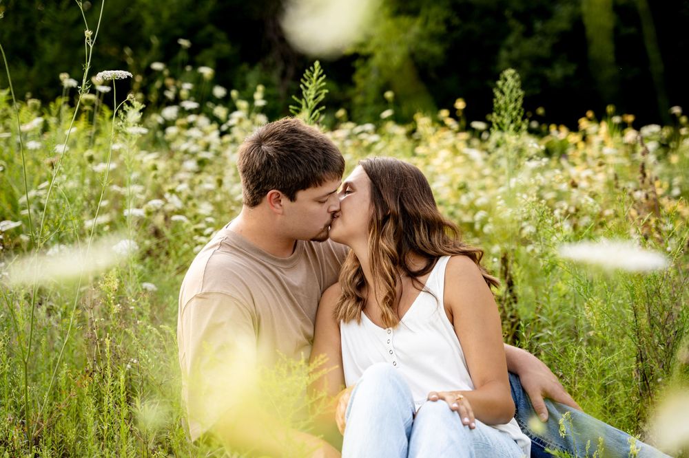 A couple shares a romantic moment in a sunlit meadow filled with white wildflowers on a summer afternoon.