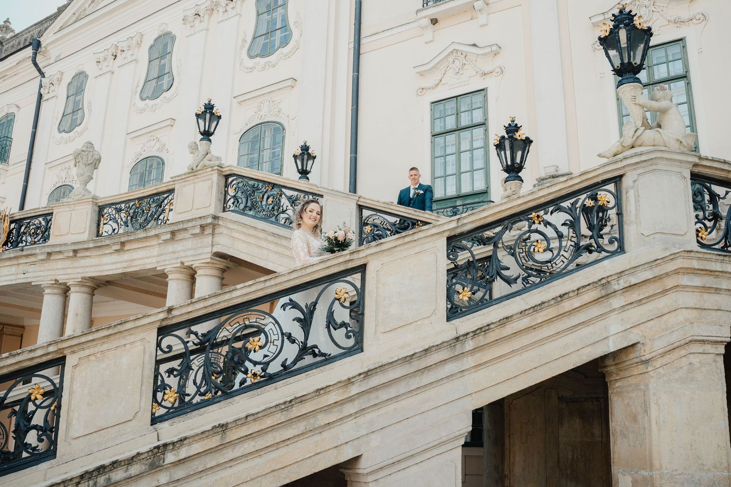 Ornate black wrought iron railings and vintage lanterns adorn the white facade of a classical European palace staircase.