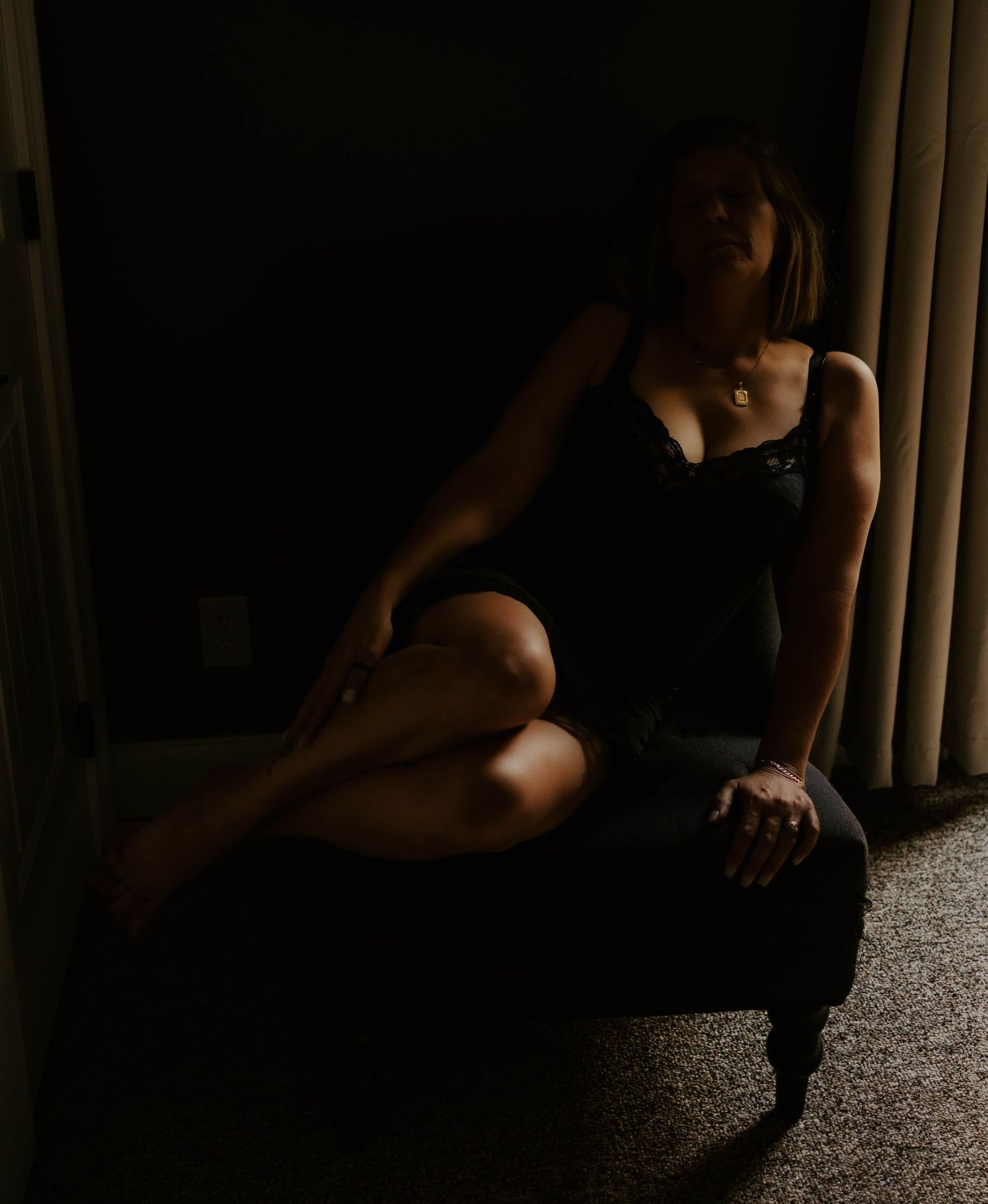 A moody boudoir portrait in dark lighting showing a figure posed dramatically on a black surface.