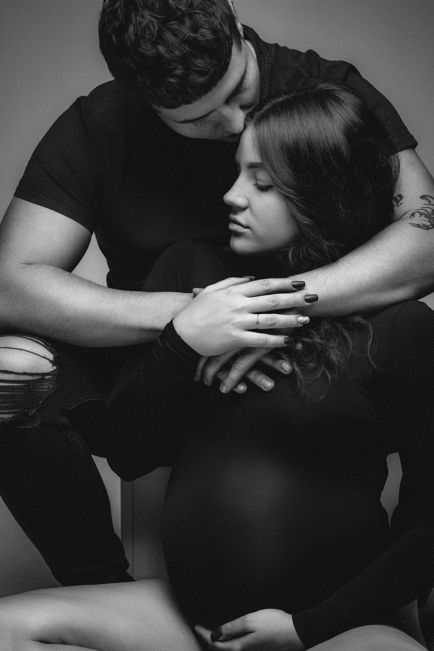Dramatic black and white maternity photo shows couple in tender embrace.