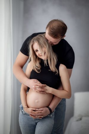 Intimate maternity photo of couple embracing while standing against grey background.