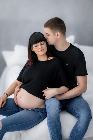 Couple sharing intimate moment on white couch during pregnancy photoshoot.