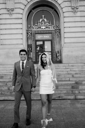 Asian groom and White bride walking down the steps of San Francisco City Hall smiling.
