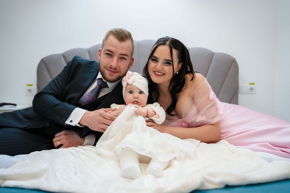 A couple lying in bed with white bedding smiles and looks at their newborn baby together.