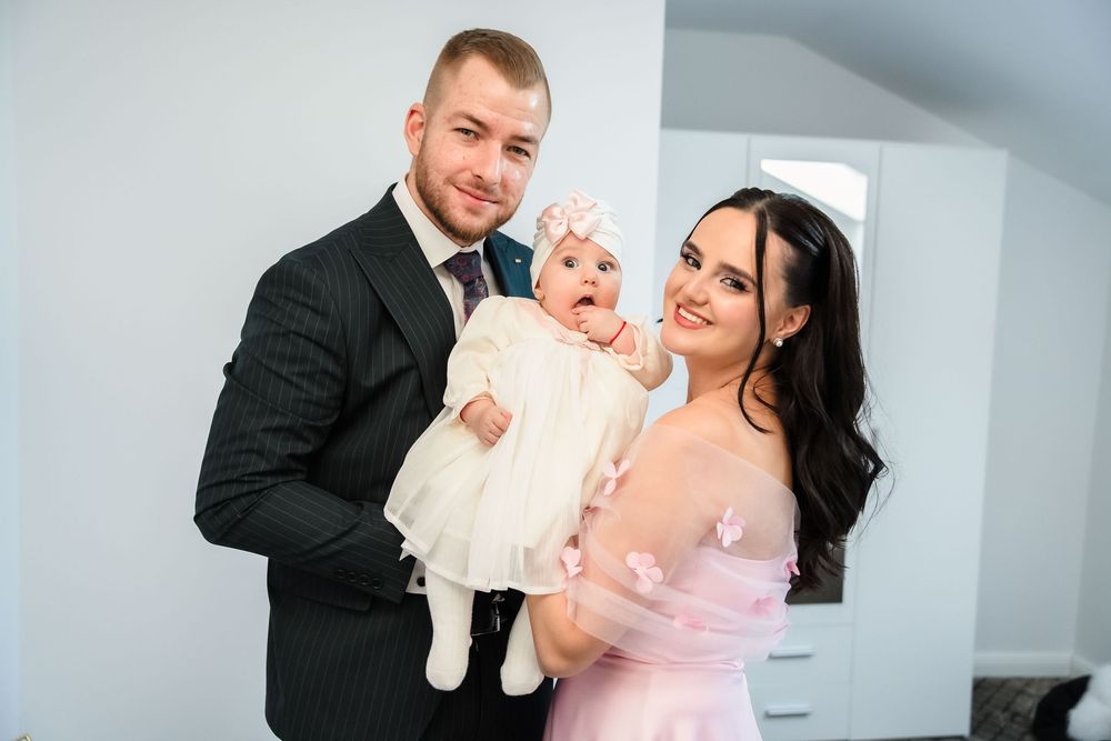 A couple in formal attire holds a baby wearing white while posing together for a family portrait session.