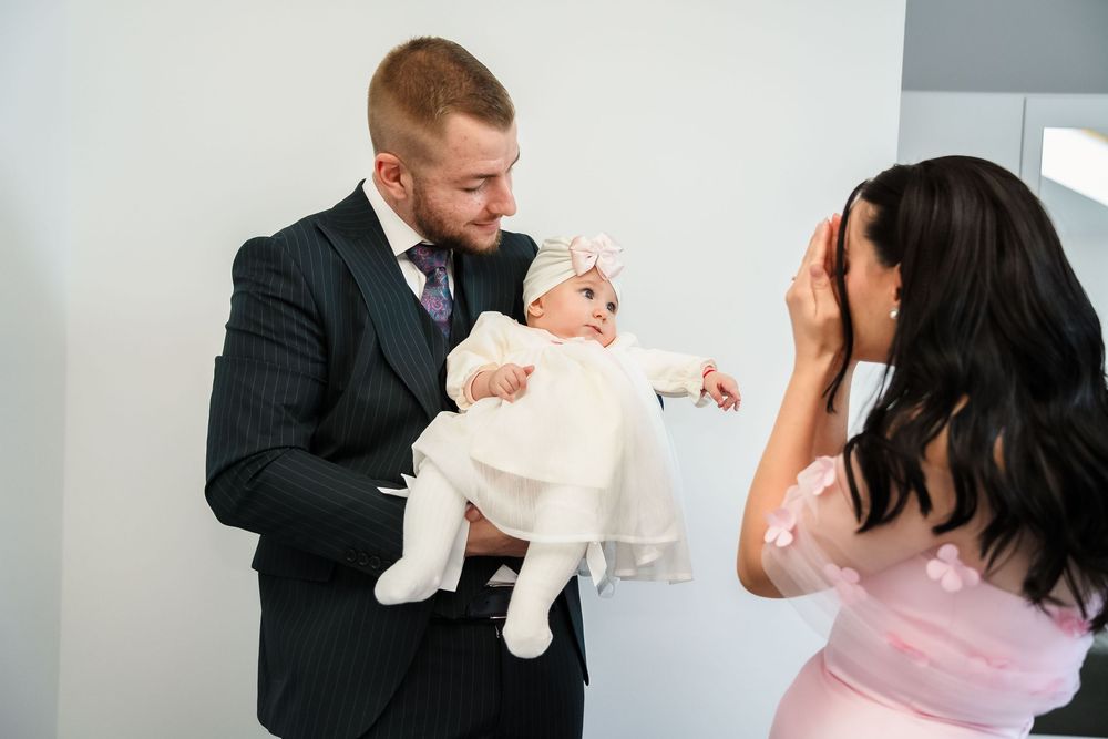 A couple in formal attire share an emotional moment with their baby dressed in white.