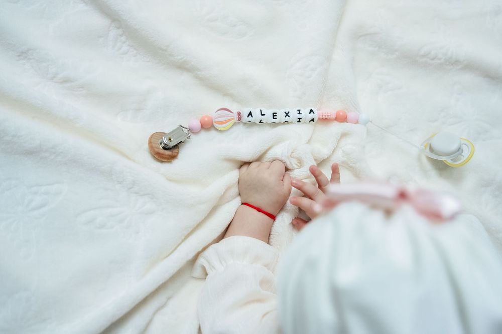 Delicate pink and white baby accessories including clothing and toys arranged on a soft white surface.