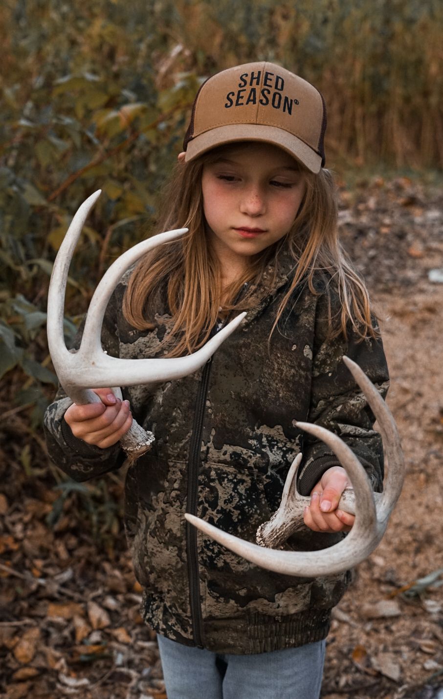 Young shed hunter examining found deer antlers in autumn woods.