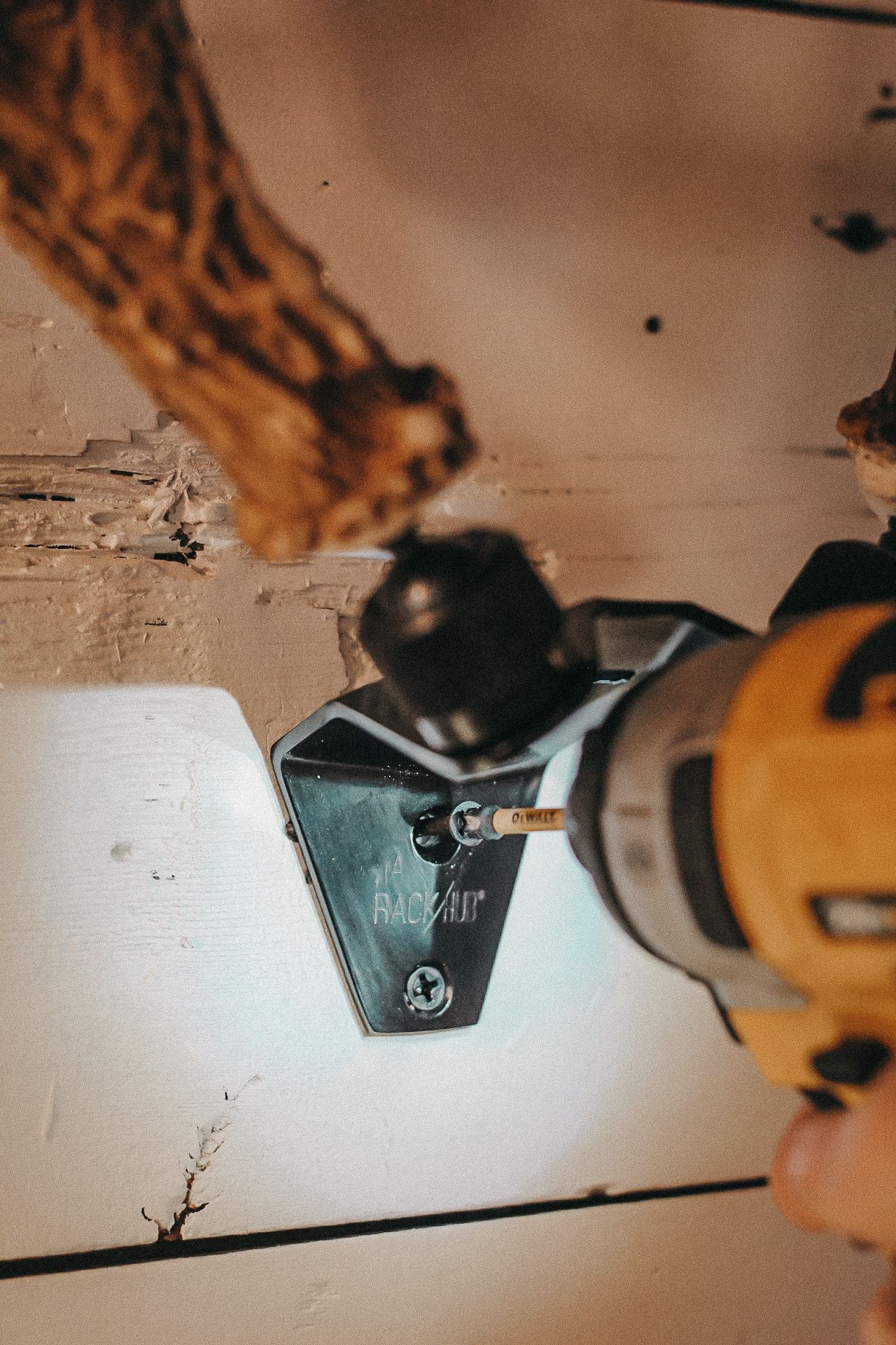 Power drill installing metal bracket on white wooden surface.