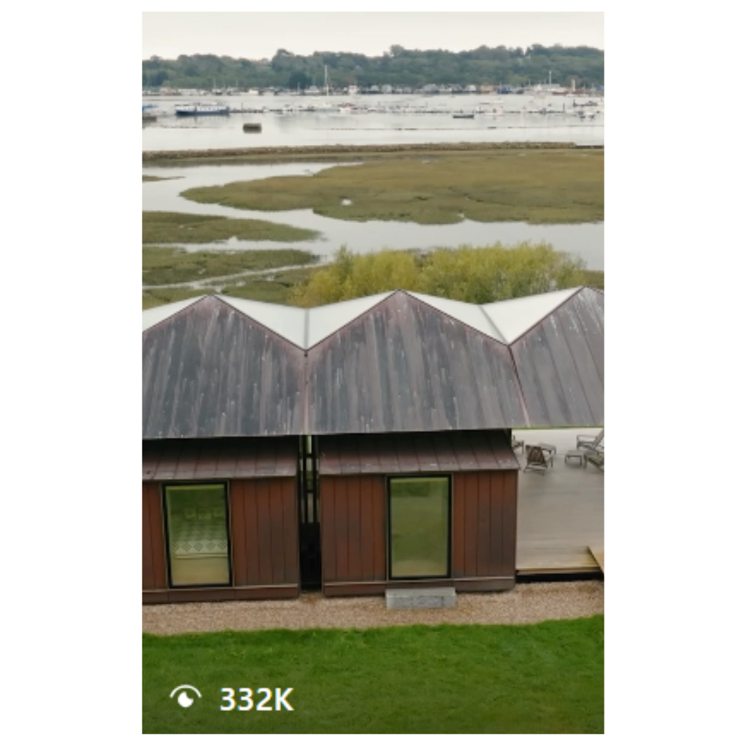 Modern waterfront building with zigzag roofline and green doors overlooking marsh landscape.