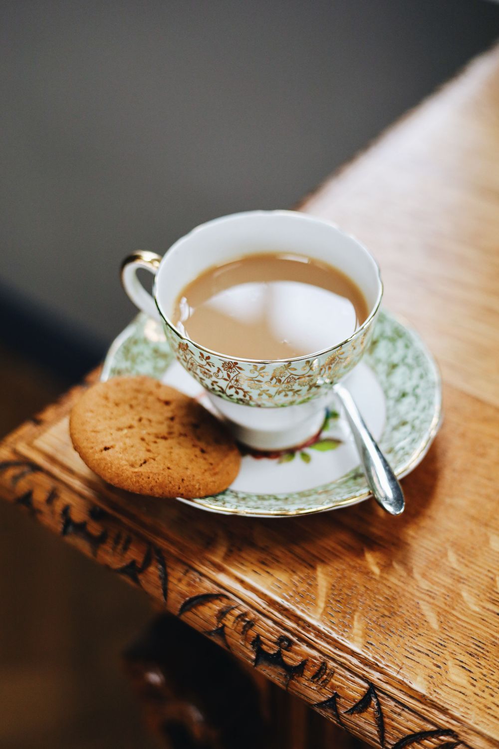 Tea cup with milk tea on wooden surface with cookies beside it.