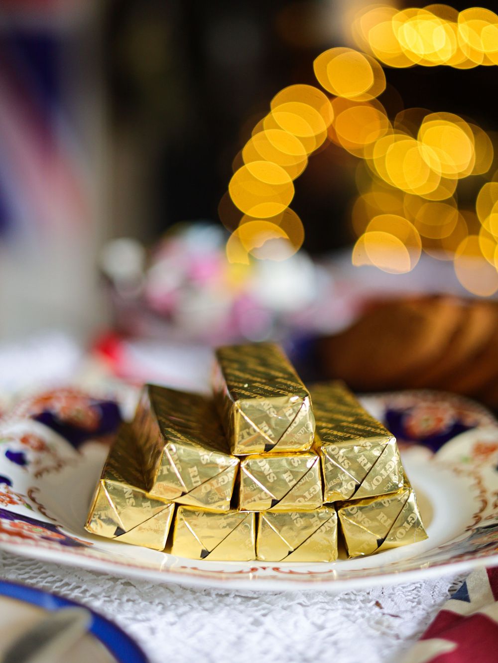 Gold wrapped chocolates arranged on decorative plate with bokeh lighting effect.