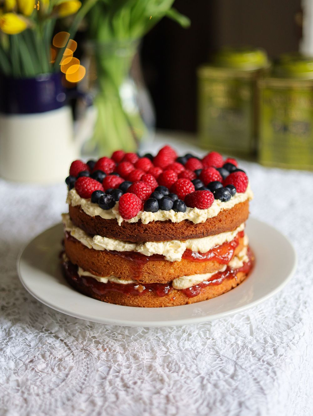 Layered chocolate cake topped with fresh raspberries and cream on white lace tablecloth.