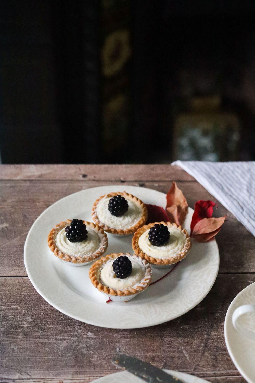 Small tartlets topped with whipped cream and blackberries served on rustic white plates.