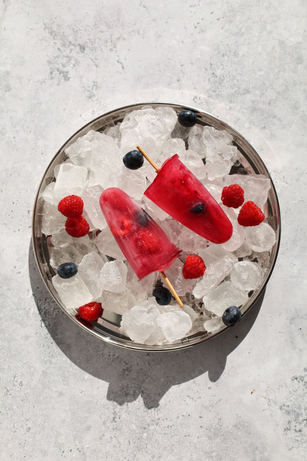 Refreshing summer drink garnished with raspberries and blueberries on crushed ice.