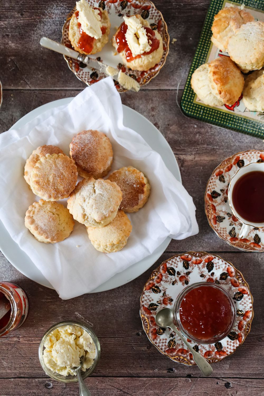 Fresh baked scones served with jam on decorative plates on a wooden table.