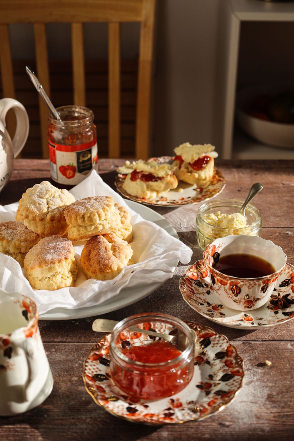 Tea service with scones and jam displayed on ornate floral dishes on a rustic wooden table.