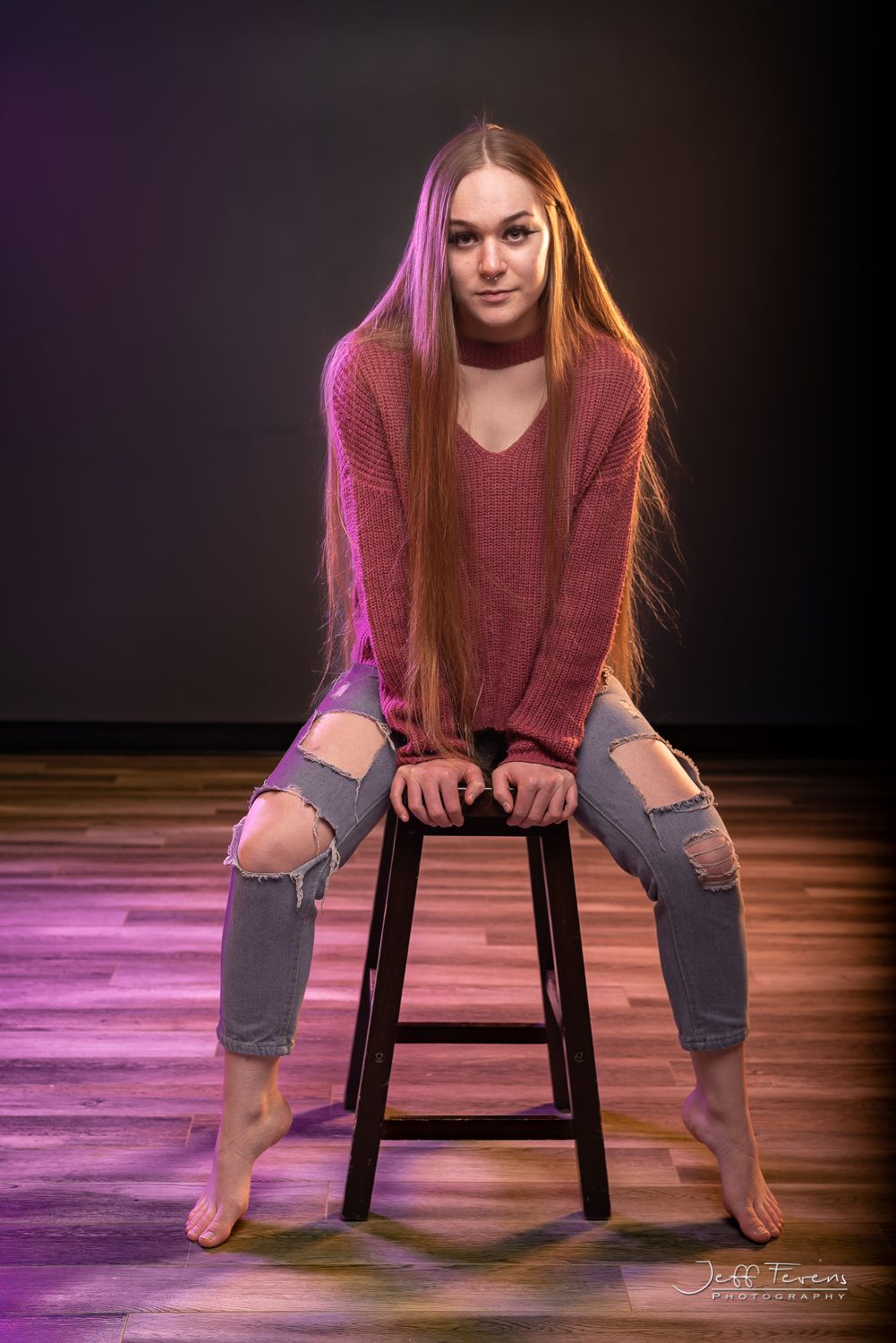 Portrait of blond woman with long hair sitting on a stool.