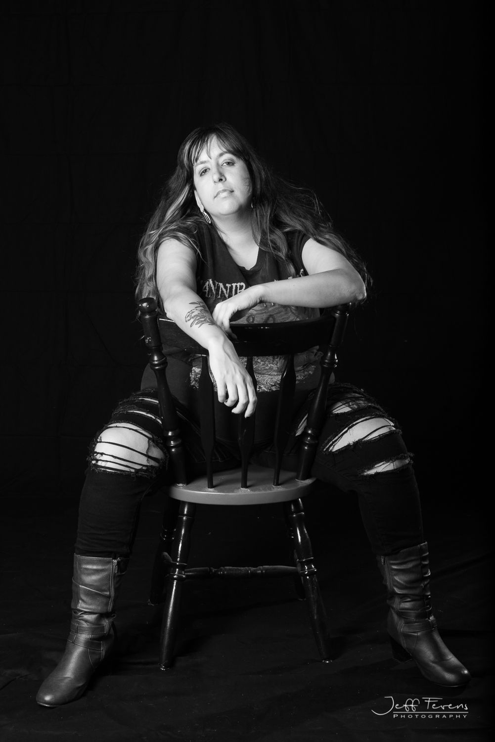 Black and White of a woman sitting in a chair in ripped jeans.
