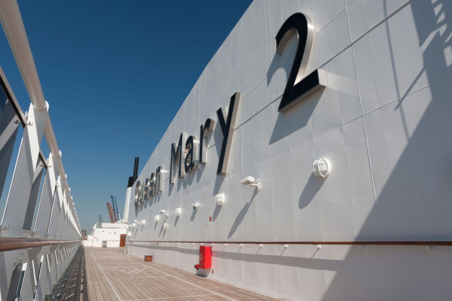 Side view of Queen Mary 2 cruise ship name painted on white hull against blue sky.