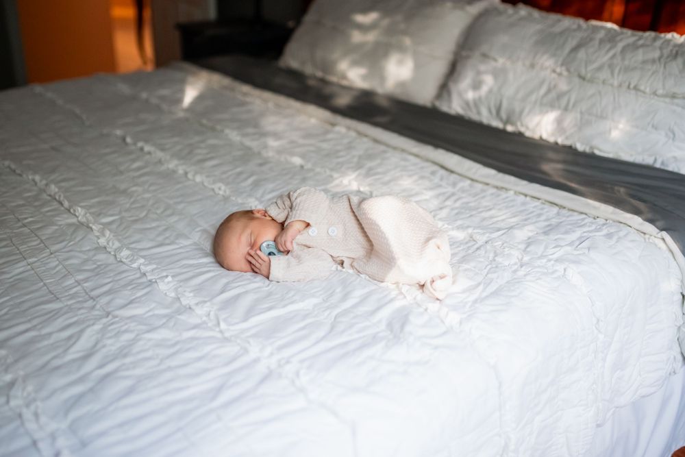 A newborn baby sleeping calmly on a white bed during a family newborn shoot.