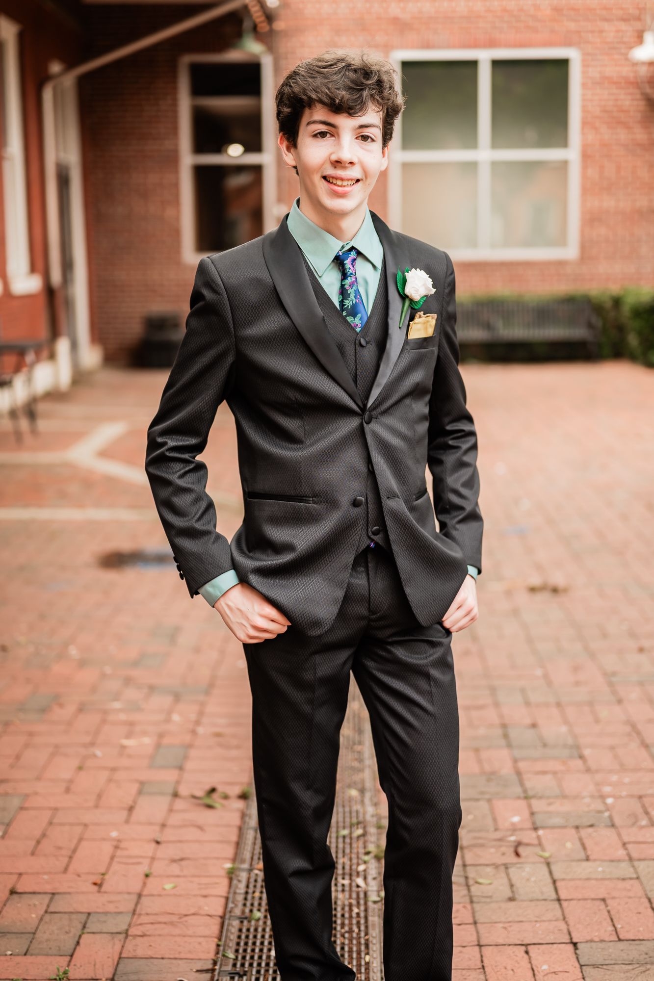 A series of four formal portraits of a child in a dark suit and boutonniere standing on brick pavement.