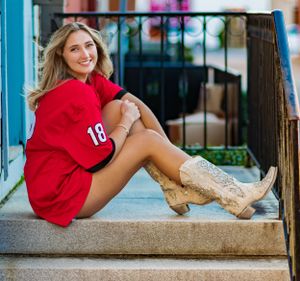 Casual senior portrait on steps wearing red sweater and beige boots.