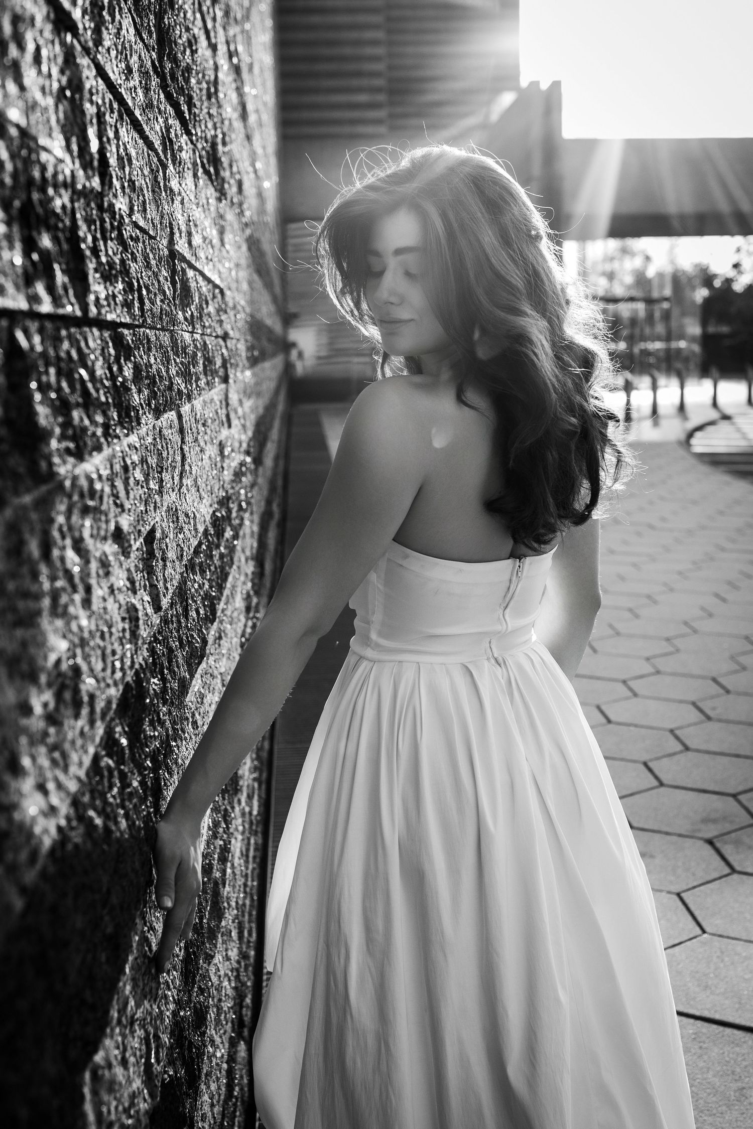 A series of black and white photos showing someone in a white dress twirling against a textured stone wall.
