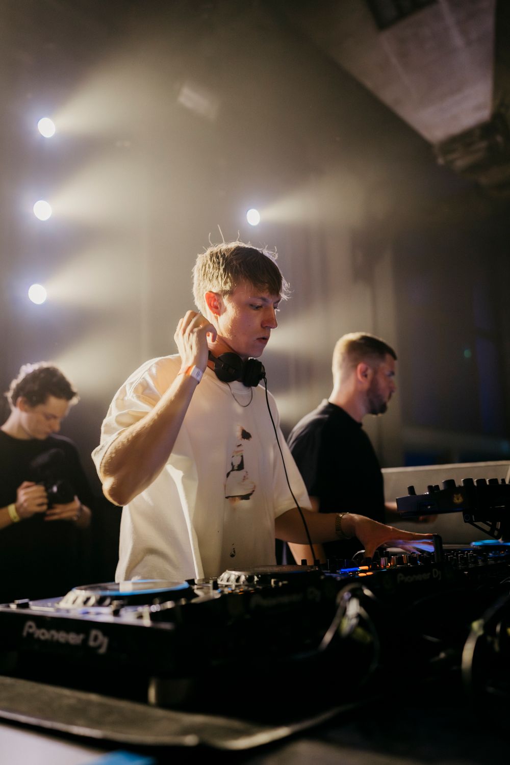 DJ performing on Pioneer equipment in a white shirt during a nightclub set.