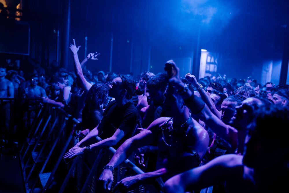 Large audience at music festival with arms raised under dramatic blue lighting.